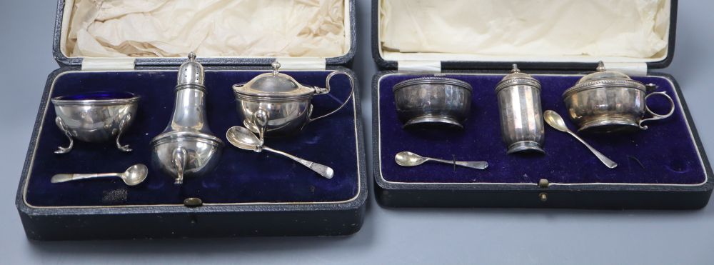 A George V three piece silver condiment set with pair of spoons and a similar three piece set with damage to mustard lid